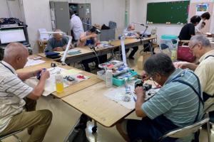 画像：入院中のおもちゃを治す先生たちの写真（拡大画像へのリンク）