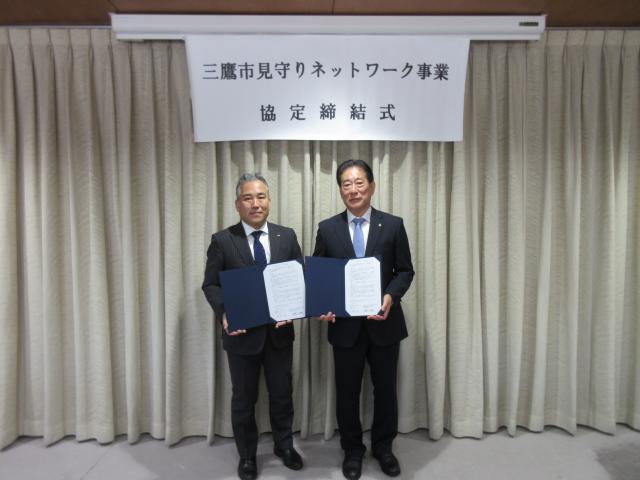 画像：協定書を手に記念撮影している宮野入多摩支社長と三鷹市長の写真