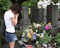 たくさんの花が供えられた墓に向かい手を合わせる女性の写真